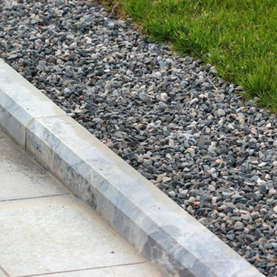 Pavement and grass separated by grass and modern looking garden edge made from stone.